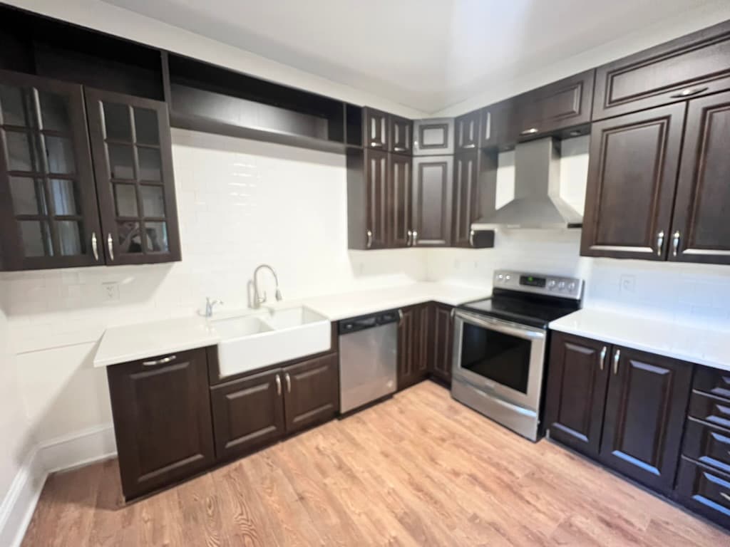 A kitchen with dark wood cabinets to the ceiling, a farmhouse sink, white tile and stainless steel appliances