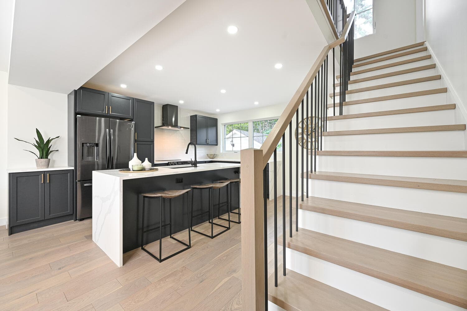 The kitchen island beside a new open staircase with light oak treads and a wood and metal railing