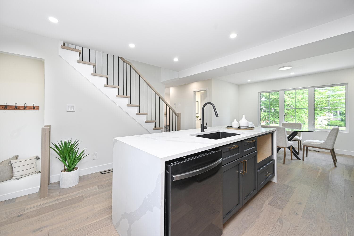 A white waterfall island with a dishwasher, looking toward the dining area and the stairs