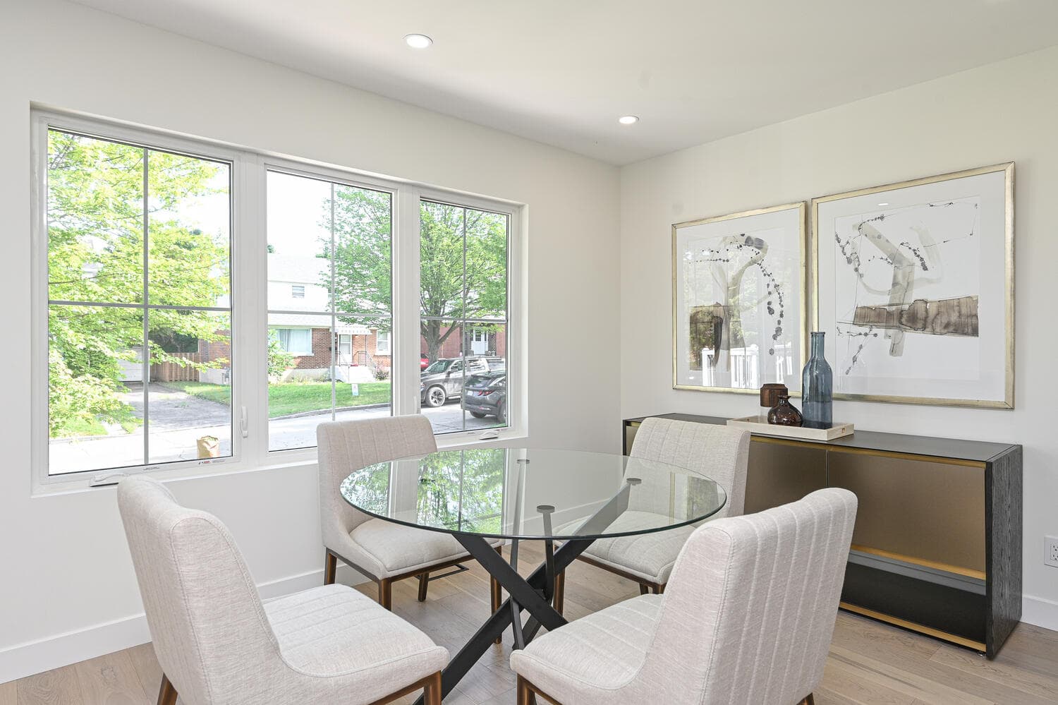 A dining area with a round glass table and a wide window onto the street trees