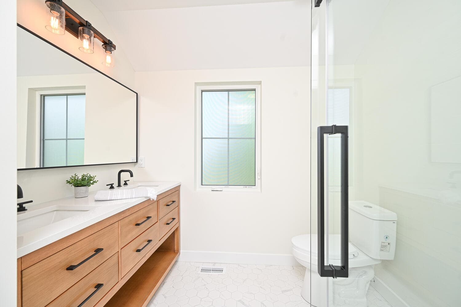 An ensuite with a wood vanity, a wide black-framed mirror and a glass shower door