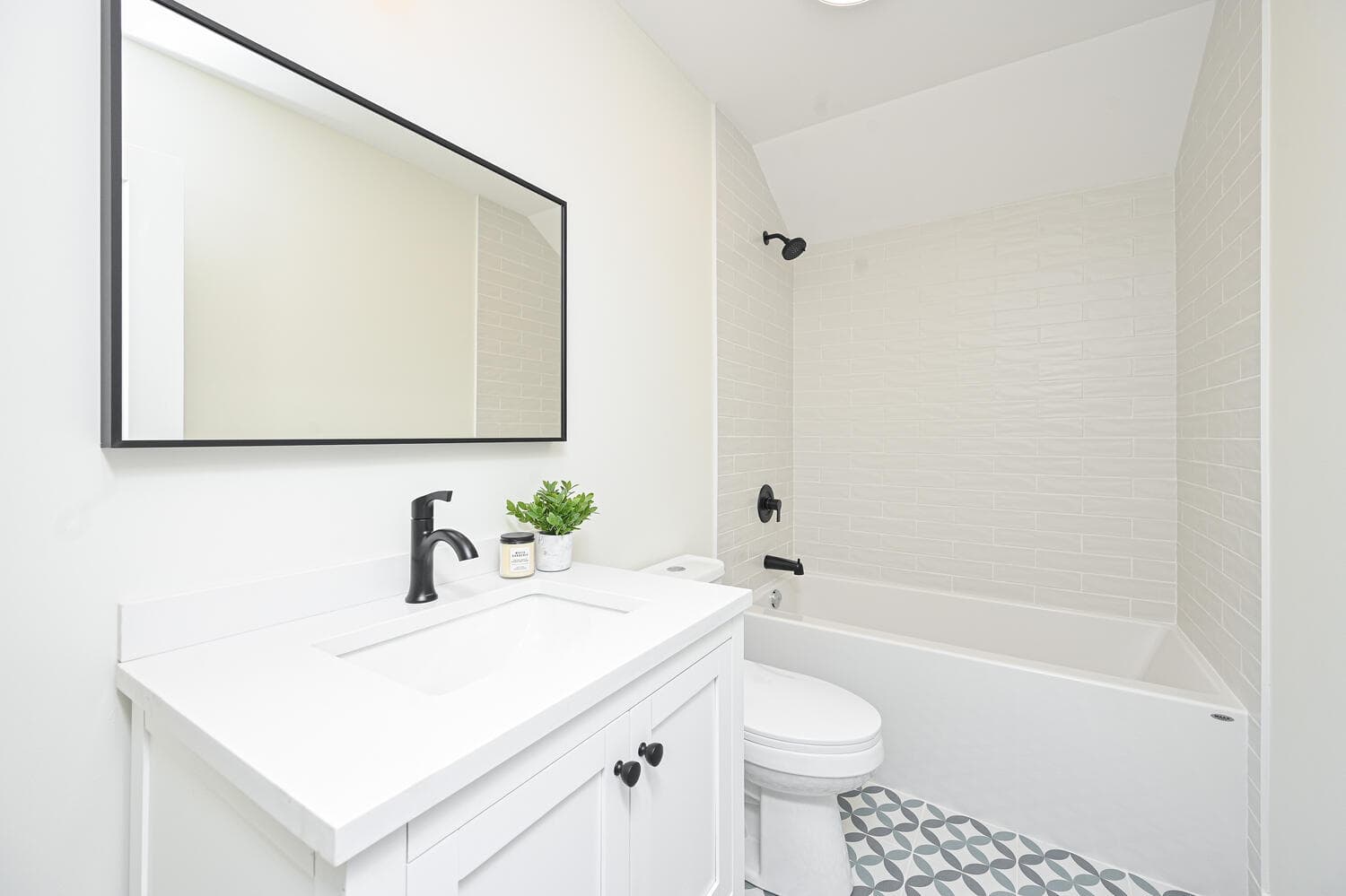A bathroom with a white vanity, a tub with a tiled surround and a patterned floor
