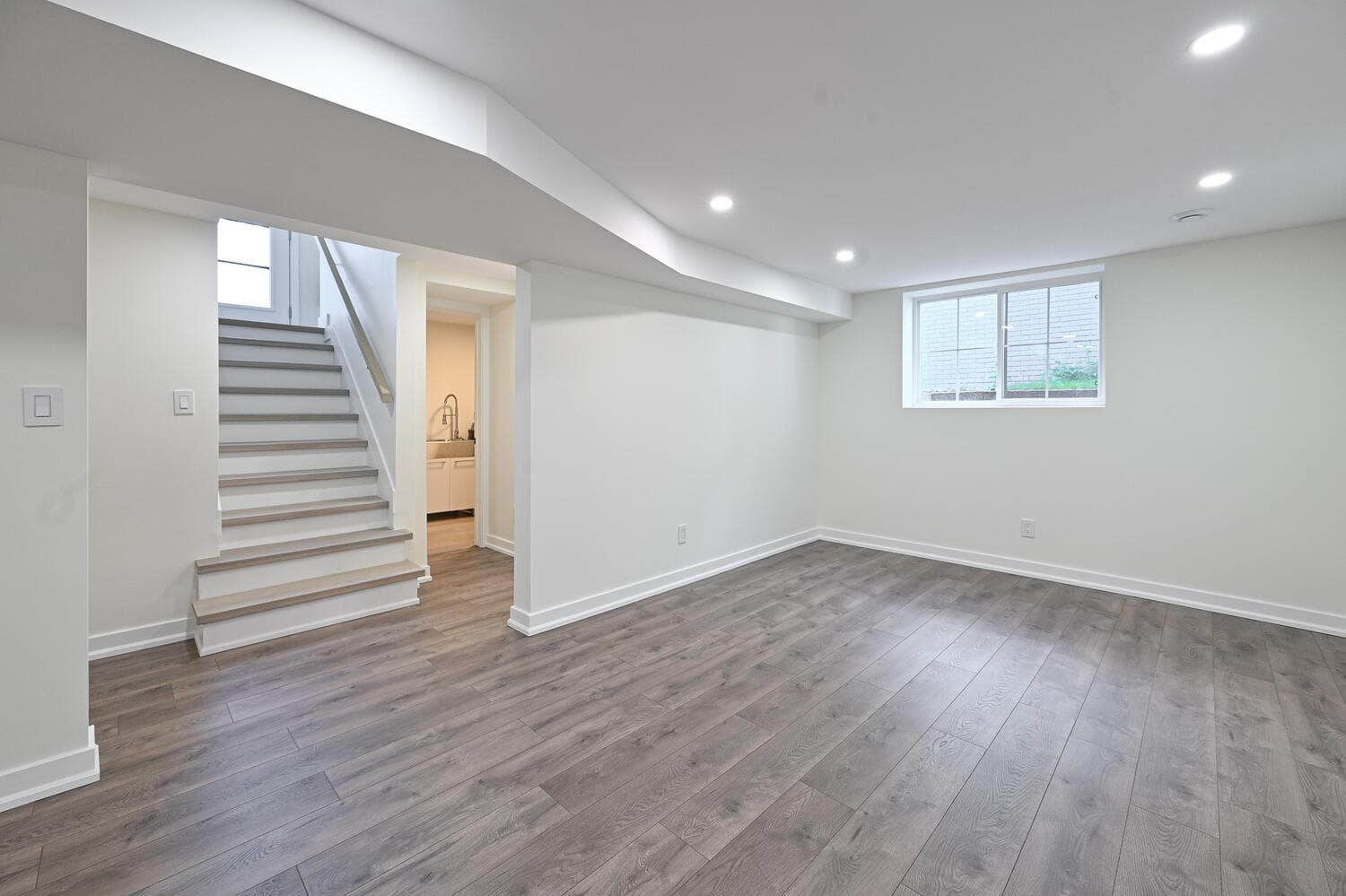 A finished basement with wide plank floors, pot lights and a lit staircase