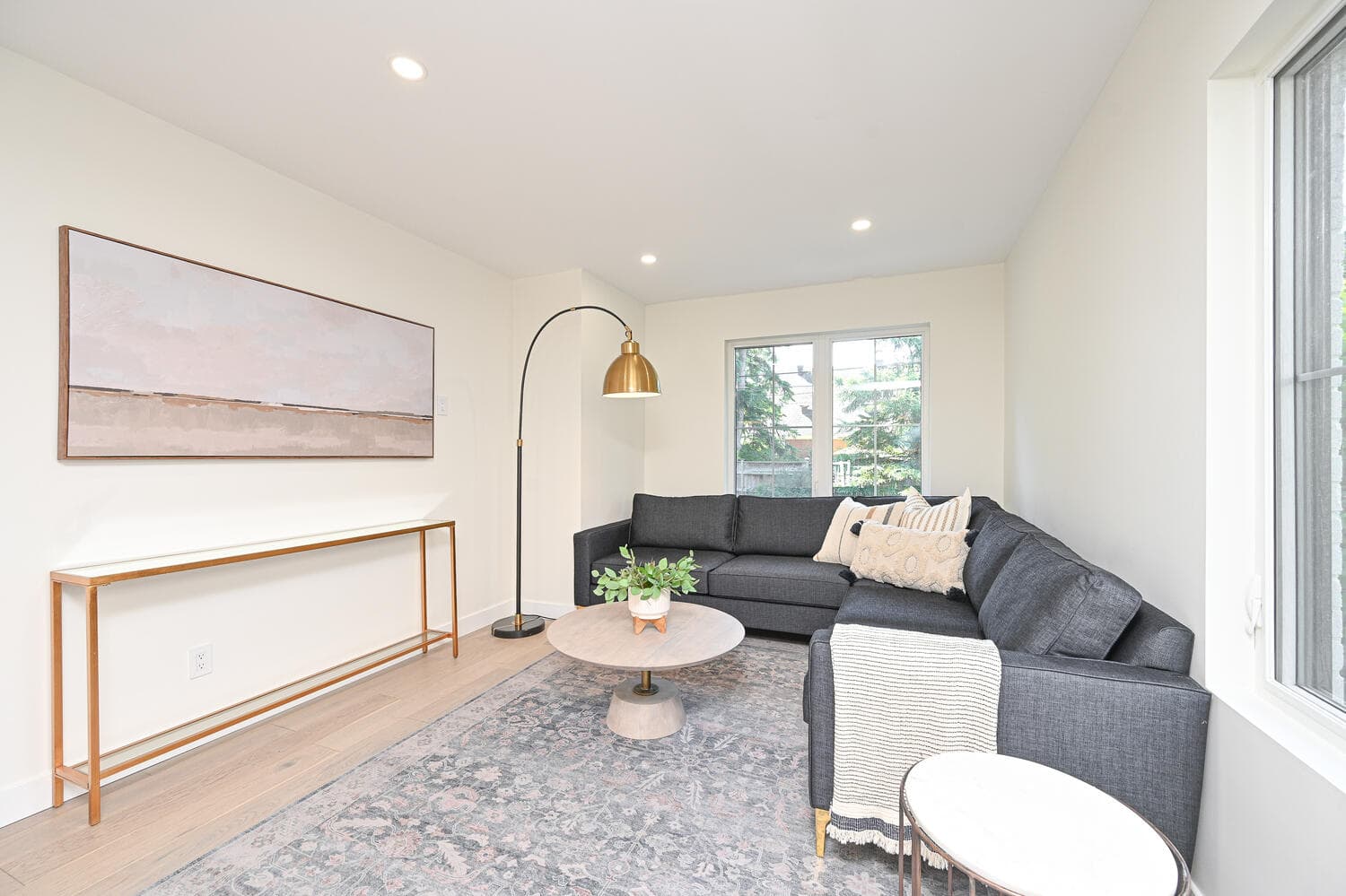 A bright living room with a grey sectional sofa, an arc floor lamp and large windows