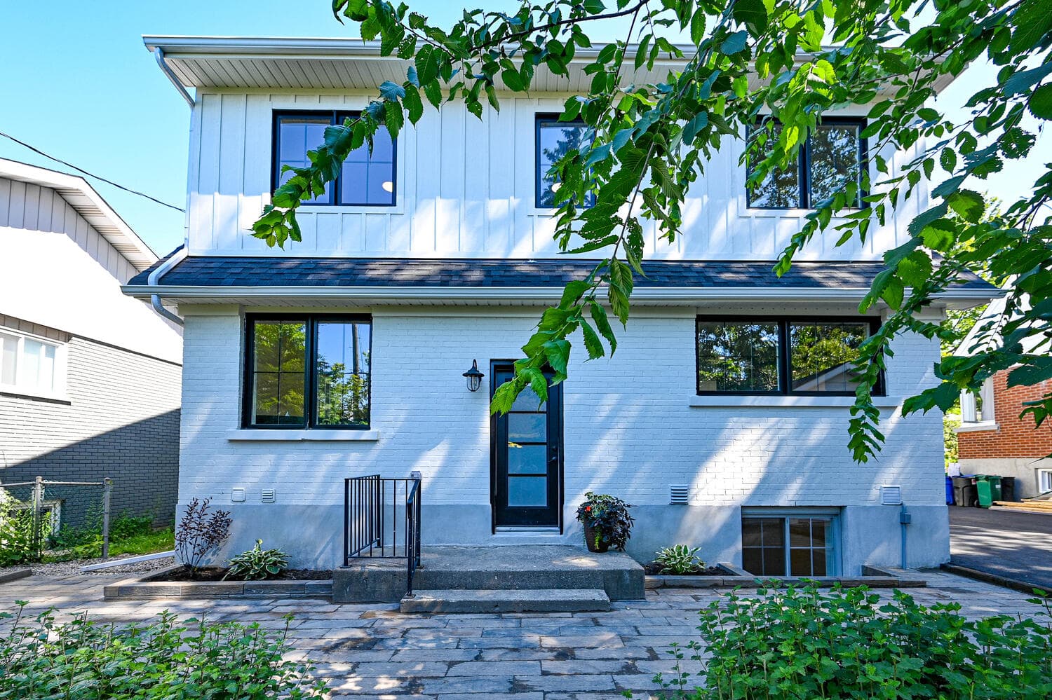 The back of the house: painted white brick, board and batten siding above, black-framed windows and a stone patio