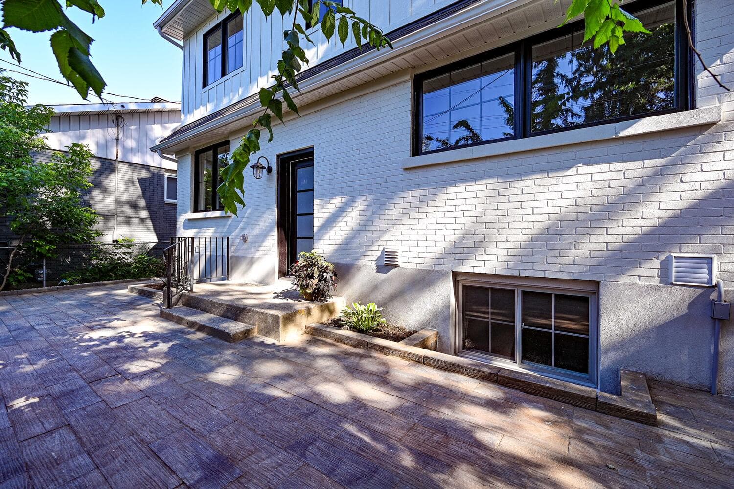 A stone patio along the back of the house, with planting beds against the brick