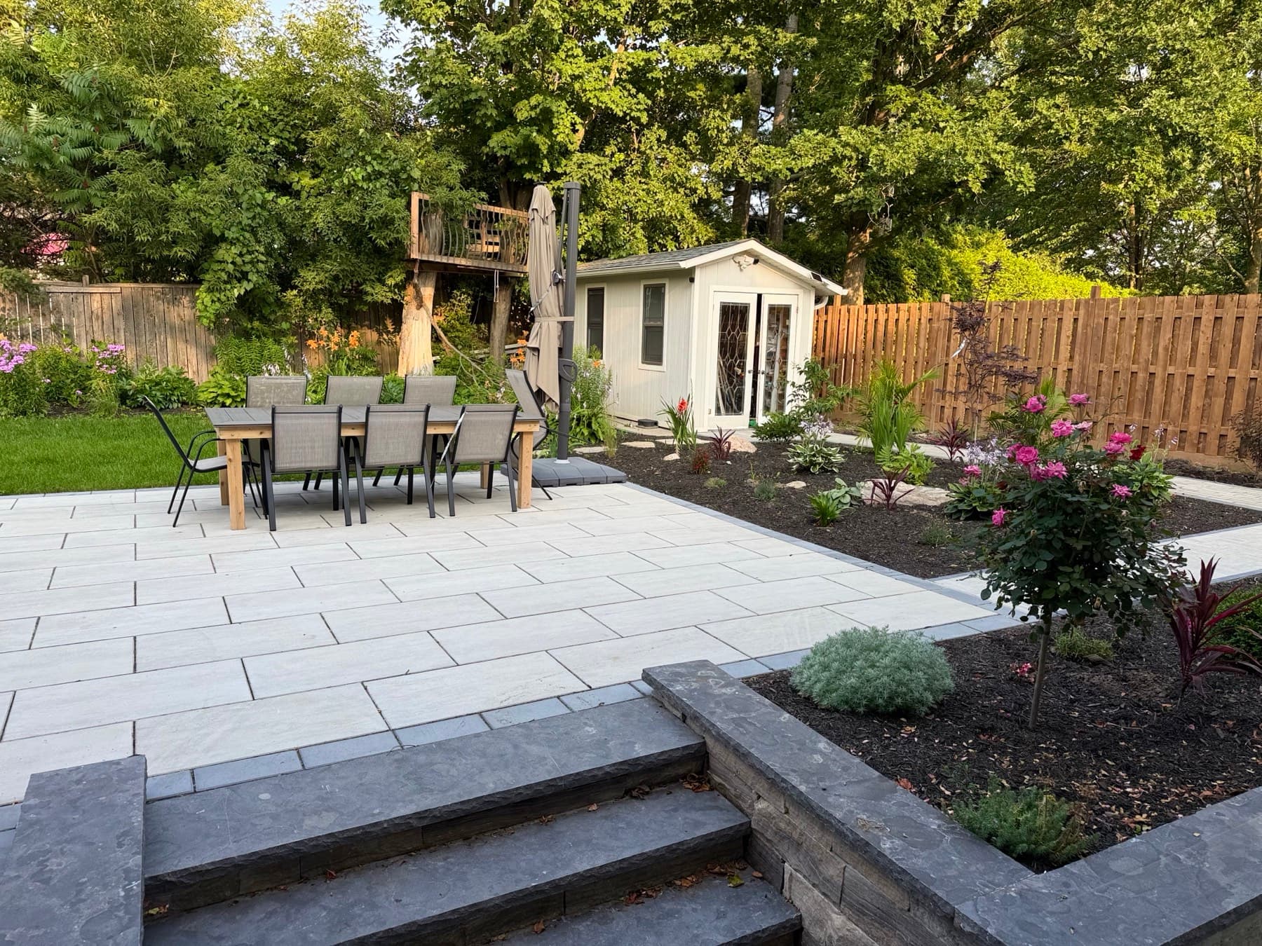 A large stone patio with an outdoor dining table, new garden beds and wide stone steps