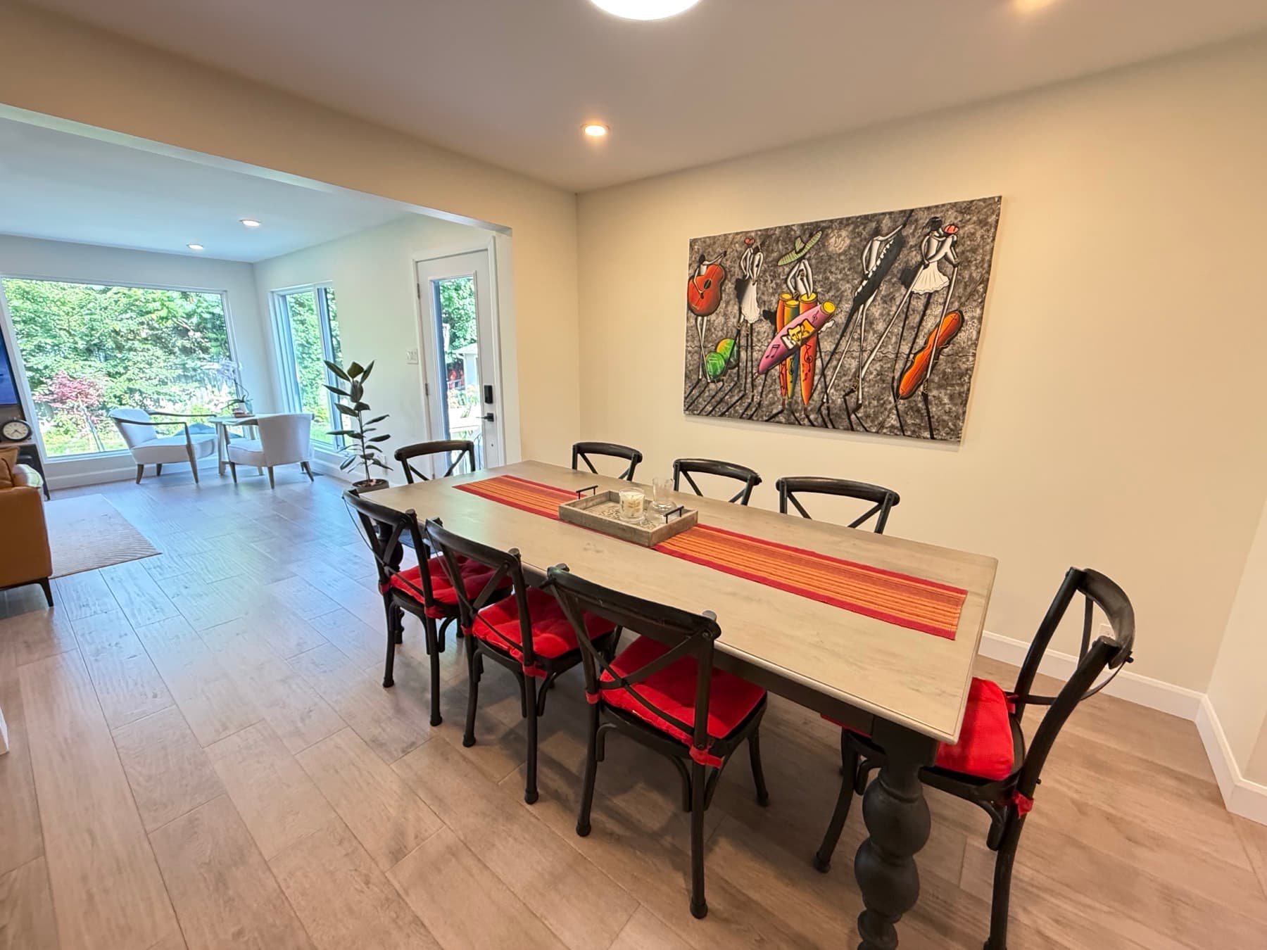 A long dining table with red cushioned chairs, open to a bright sitting area with a glass door to the garden
