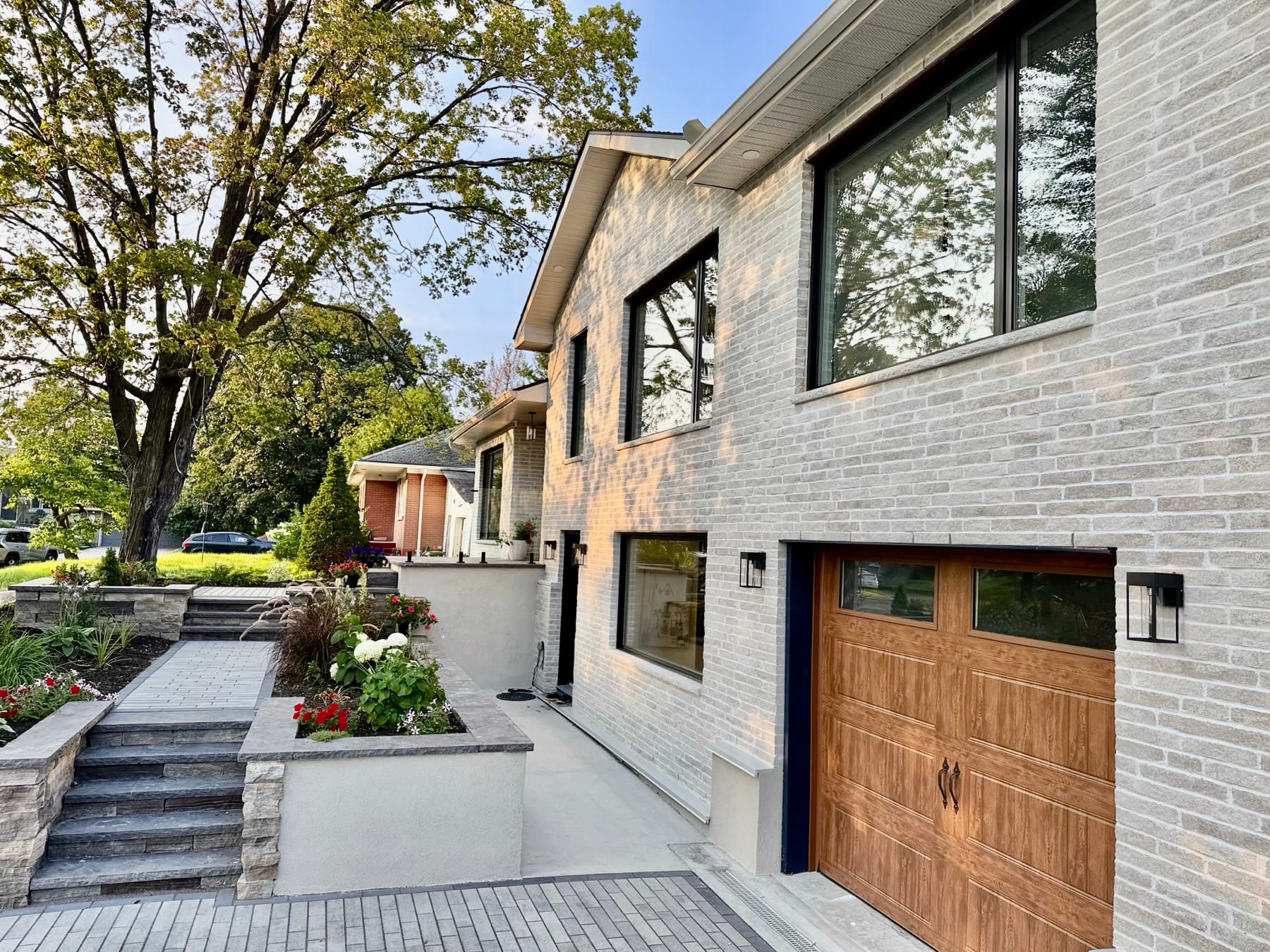 The side of the house: light brick, large black-framed windows, a wood-look garage door and raised garden beds
