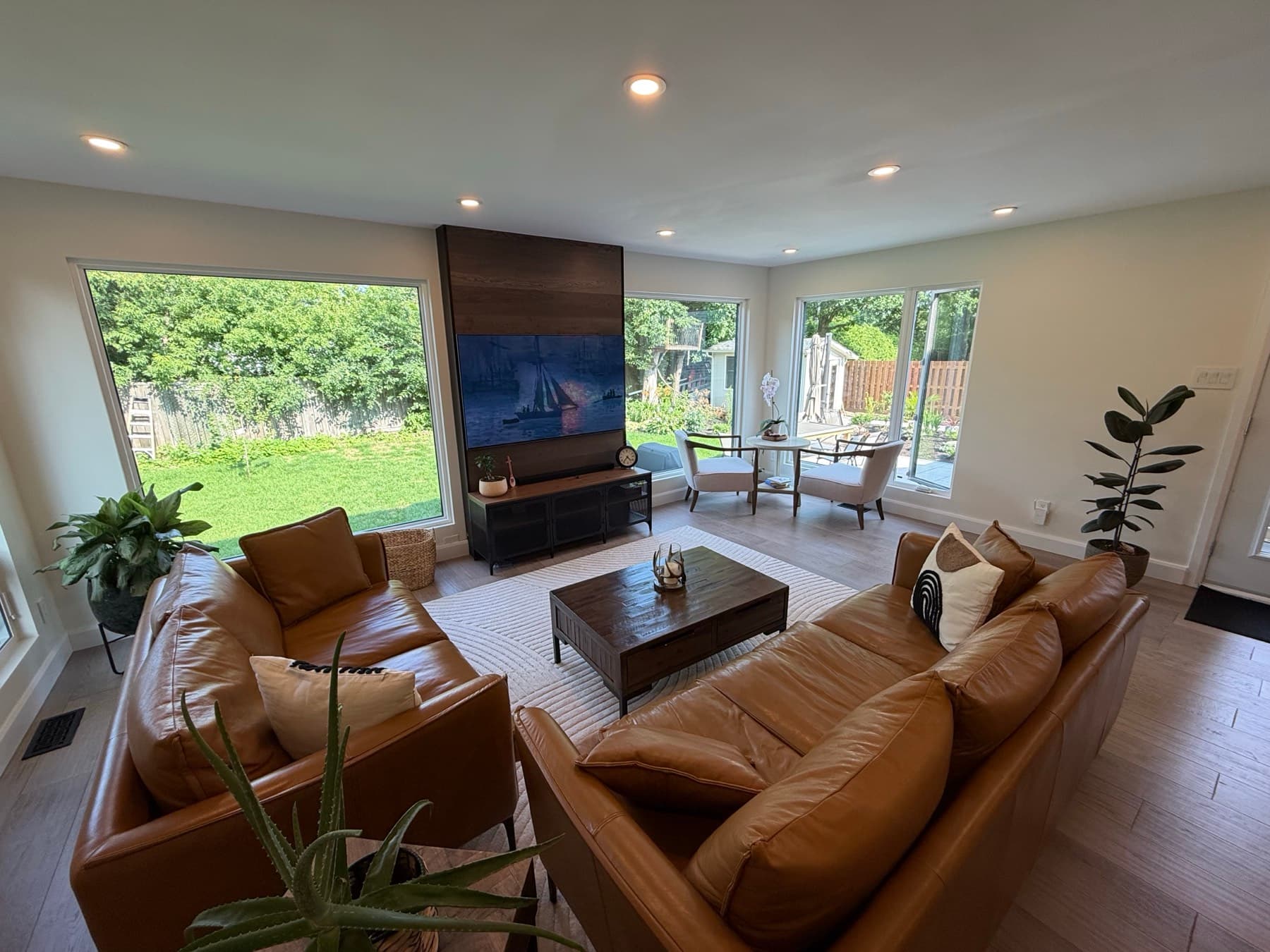 A living room with two leather sofas, a dark wood feature wall and large windows onto the lawn and back garden