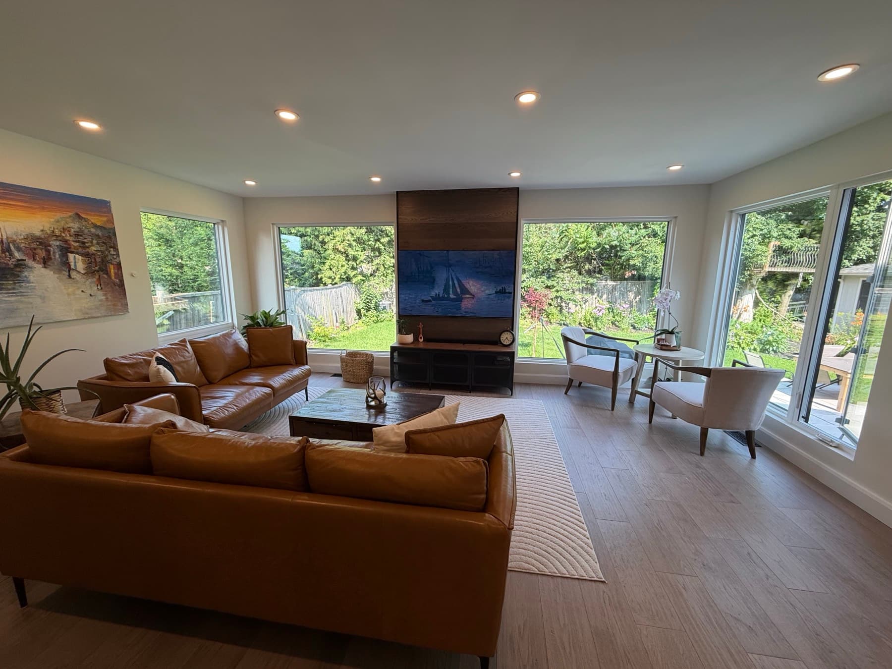 A living room with leather sofas, a wood feature wall and large windows on three sides looking onto the garden
