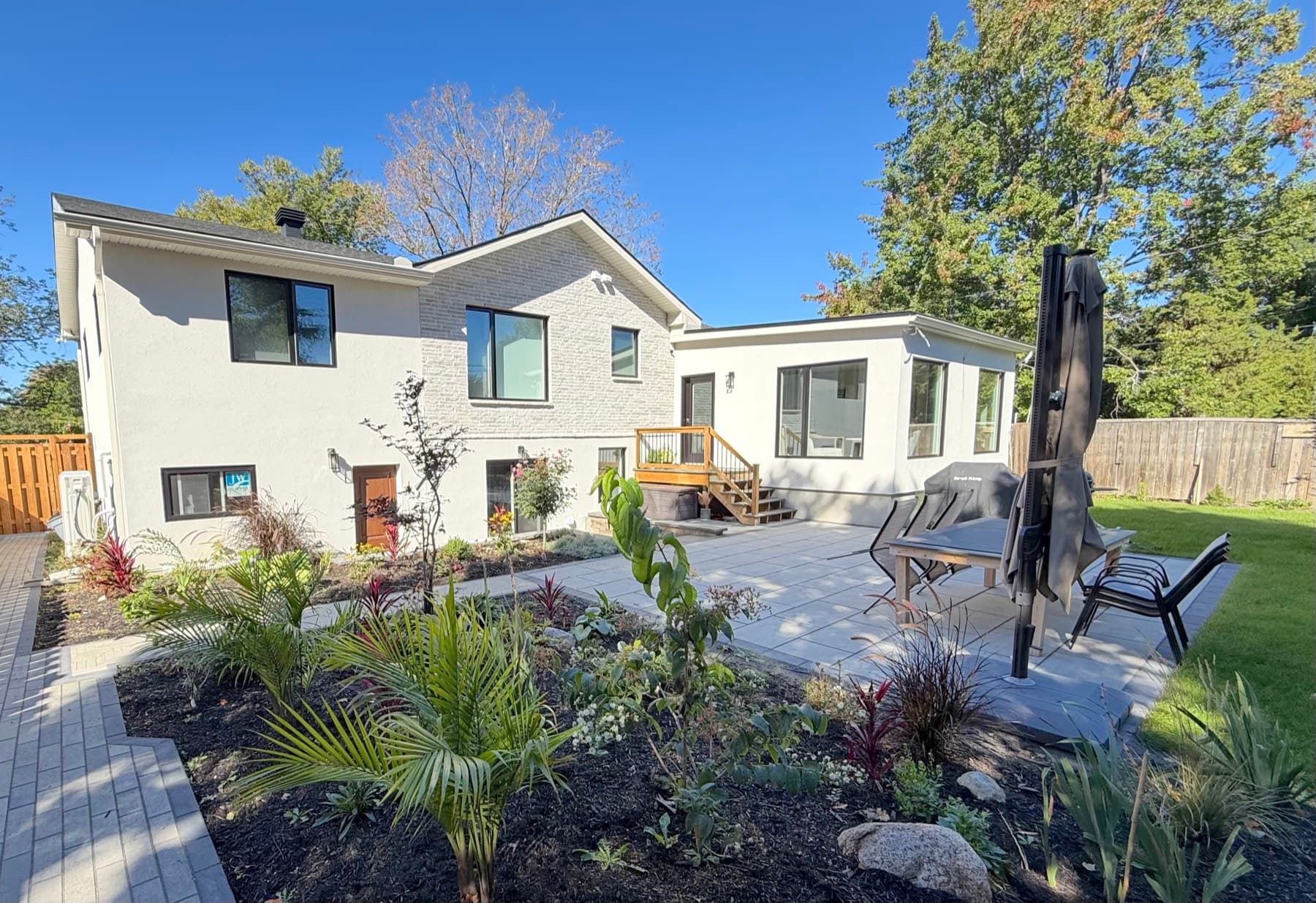 The same view after: stucco and brick, large black-framed windows, a new stone patio and gardens