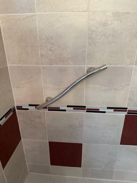 A curved stainless steel grab bar mounted on a tiled shower wall