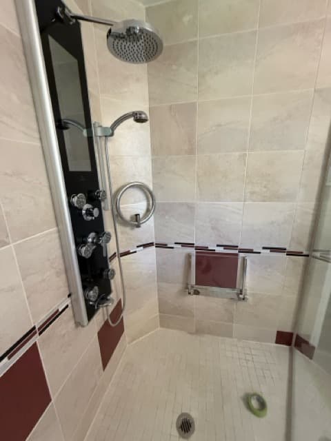A tiled shower with a handheld shower on a slide bar and a fold-down seat