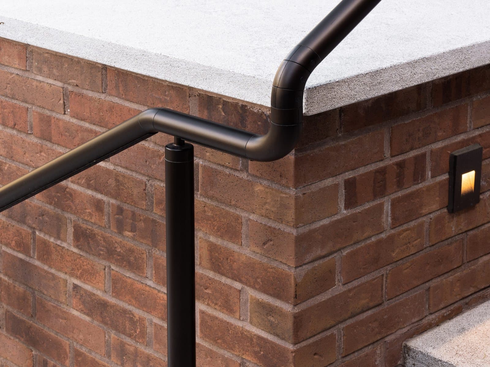 A black aluminum handrail on a post, turning along a brick wall beside stone steps