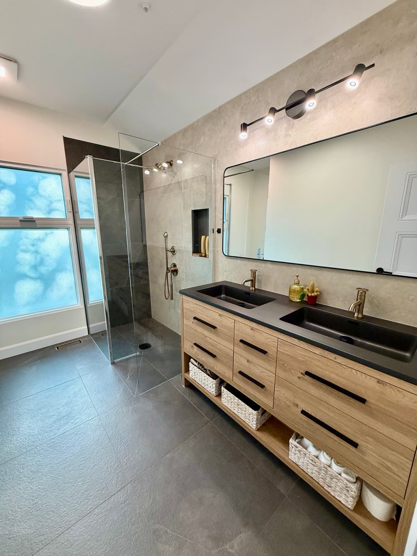 A curbless walk-in shower with a glass panel beside a wood double vanity