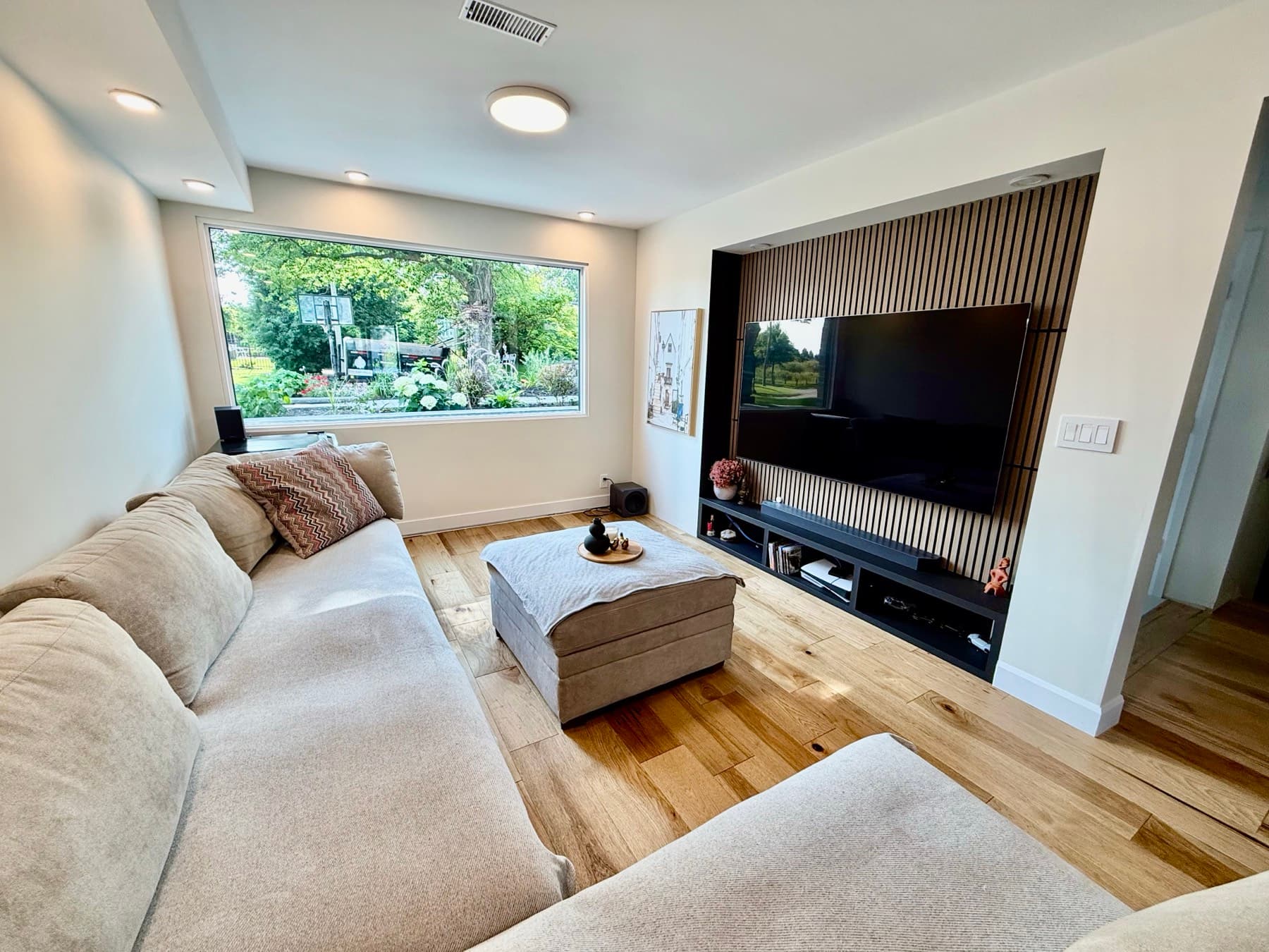 A family room with a slatted wood media wall and a large window onto the garden
