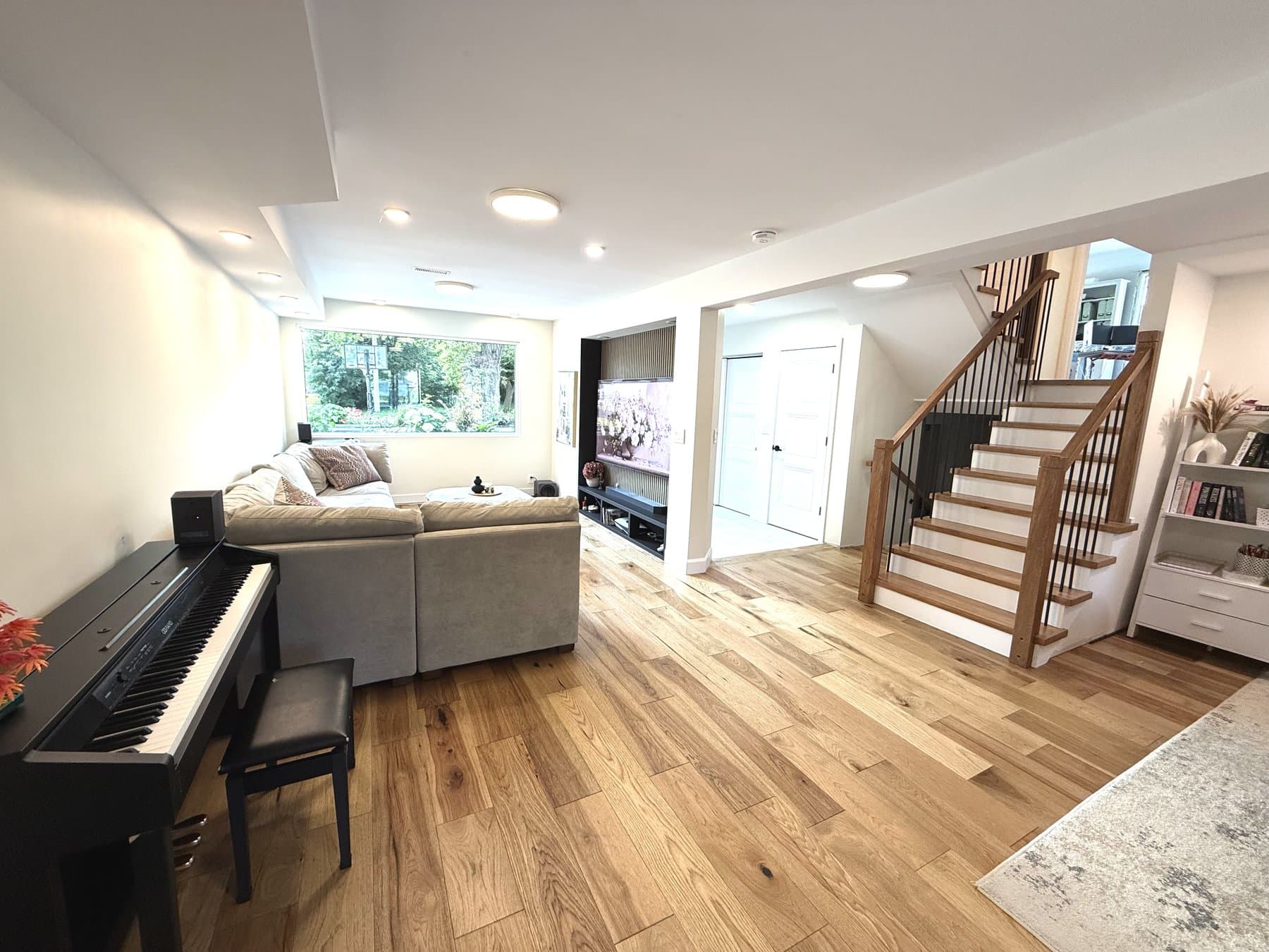 A family room with oak floors, a sectional sofa, a slatted media wall and a new wood staircase with black metal spindles