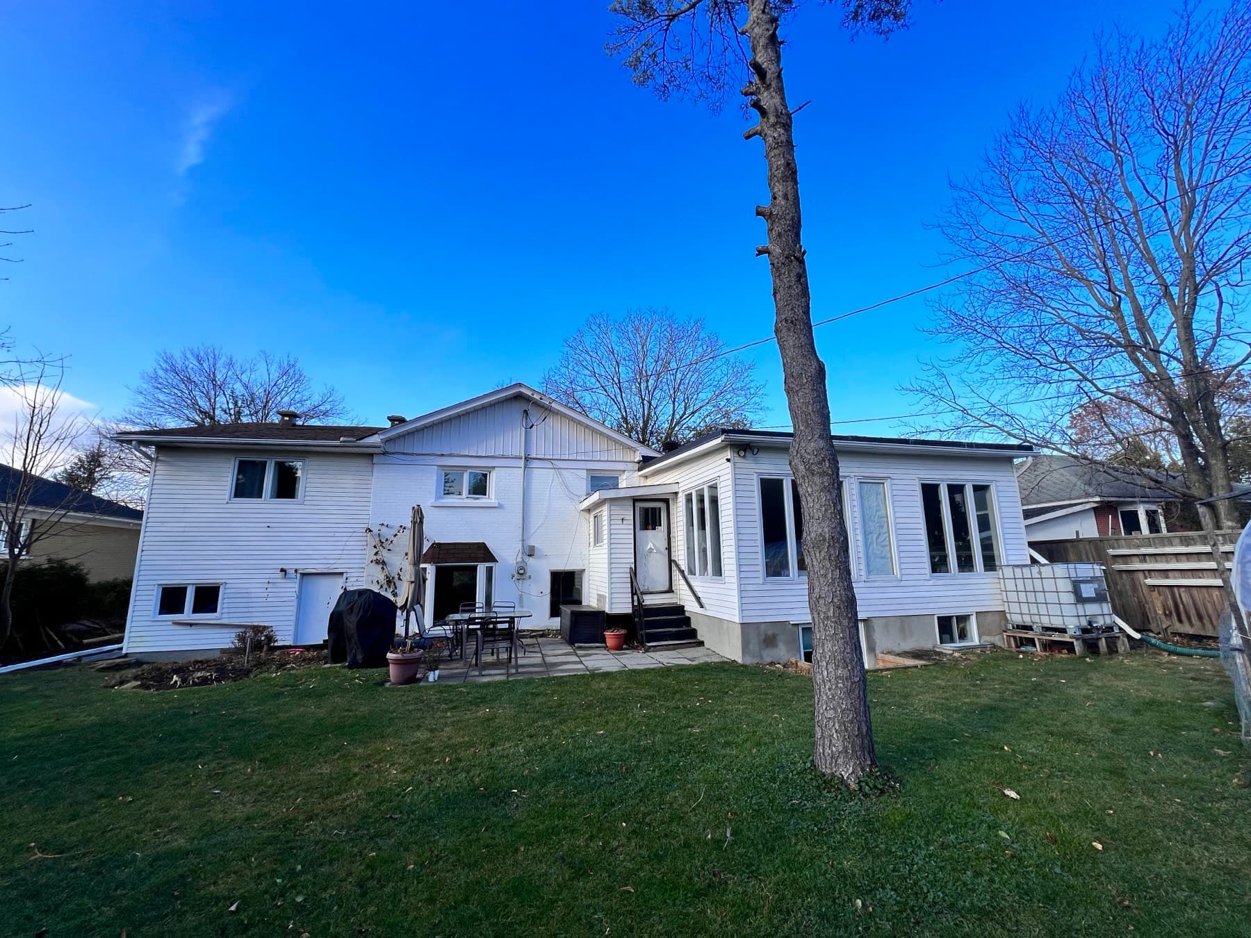 The back of the split-level before the renovation: white siding, small windows and a worn patio